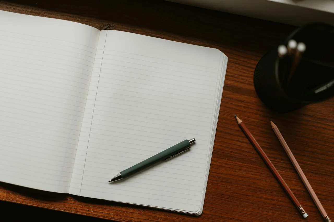 Caderno aberto com caneta e lápis sobre uma mesa de madeira